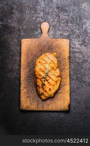 Roasted chicken breast on wooden cutting board on dark rustic background, top view