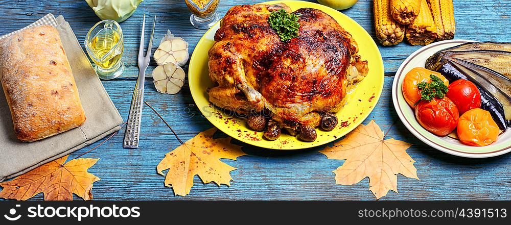 Roasted chicken on wooden plate. Kitchen table with baked chicken in vegetables and strewn with autumn leaves
