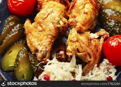 Roasted chicken pieces served with pickles. Food background. Tasty baked chicken and pickles.