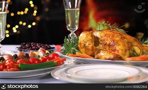 Roasted chicken ready to be served on Christmas festive table with champagne near Christmas tree and fireplace. Dolly shot