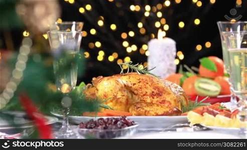 Roasted chicken ready to be served on Christmas festive table with champagne near Christmas tree. Dolly shot