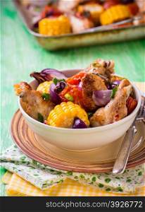 Roasted chicken with vegetables in bowl. Chicken wings, tomato, corn and onion. Green background, selective focus, rustic