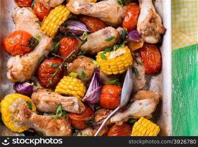 Roasted chicken with vegetables in metal baking tray. Chicken wings, tomato, corn and onion. Green background, selective focus, closeup, top view