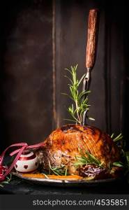 Roasted Christmas ham with fork at wooden background, side view