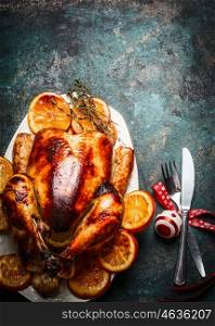 Roasted Christmas turkey with orange slices served with festive decoration on dark rustic background, top view