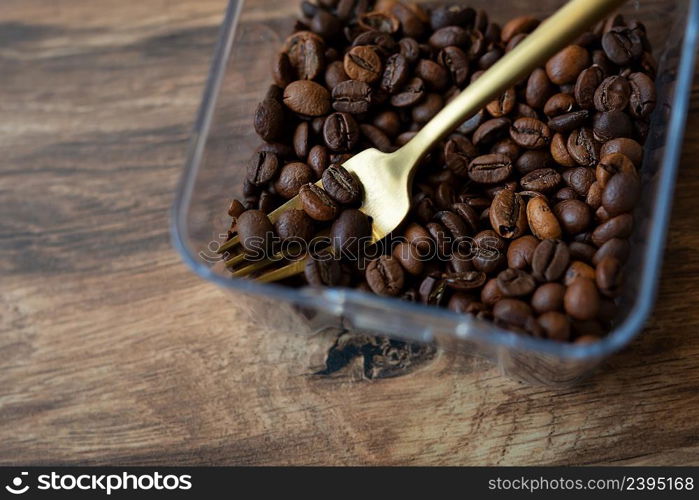 Roasted coffee bean in a plastic box along with a fork, close-up, top view. The concept of making coffee. Roasted coffee bean in a plastic box along with a fork, close-up, top view. The concept of making coffee.