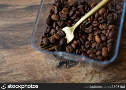 Roasted coffee bean in a plastic box along with a fork, close-up, top view. The concept of making coffee. Roasted coffee bean in a plastic box along with a fork, close-up, top view. The concept of making coffee.