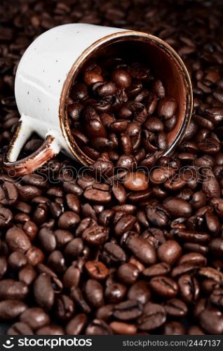 Roasted coffee beans and coffee cup on texture of coffee beans ready to drink, selective focus. Roasting and preparing coffee, vertical frame