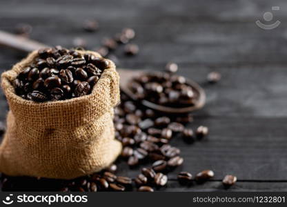 Roasted coffee beans are placed in a small sack, placed on a black wooden table.