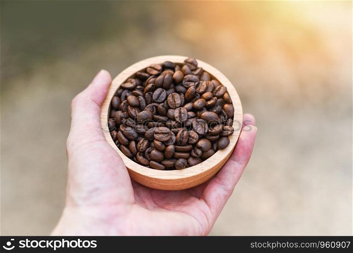 Roasted coffee beans hold in hand / Close up of coffee beans on wooden bowl