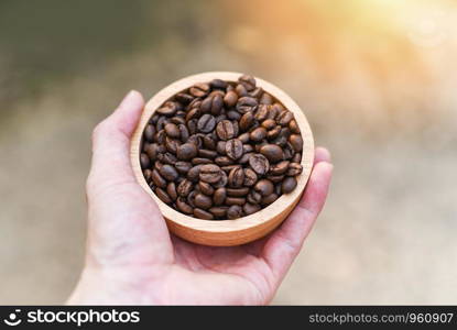 Roasted coffee beans hold in hand / Close up of coffee beans on wooden bowl