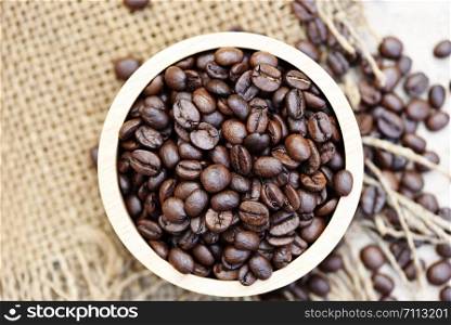 Roasted coffee beans in a wooden bowl on sack background , top view