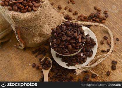 Roasted coffee beans in jute sack and cup on wooden background