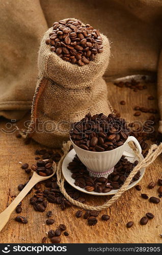 Roasted coffee beans in jute sack and cup on wooden background