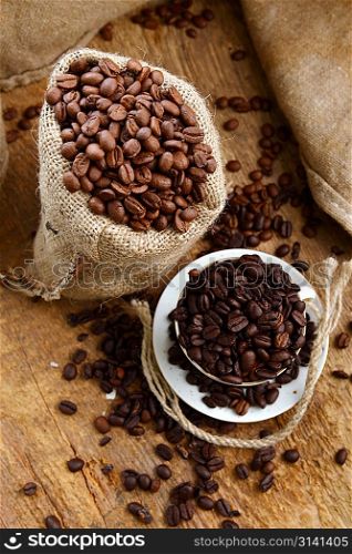 Roasted coffee beans in jute sack and cup on wooden background