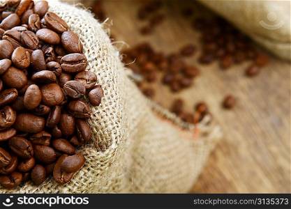 Roasted coffee beans in jute sack on wooden background