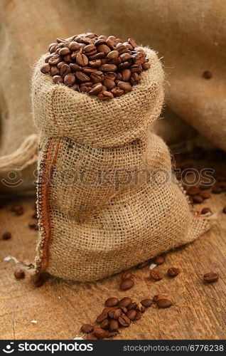 Roasted coffee beans in jute sack on wooden background