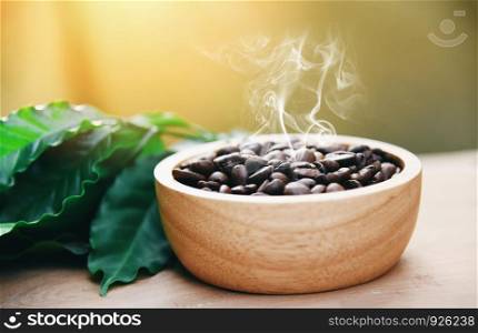 Roasted coffee beans on wooden bowl with green coffee leaf on wooden table background