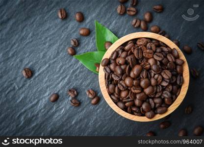 Roasted coffee beans on wooden bowl with green leaf and dark background - top view