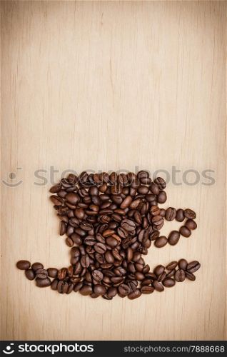 Roasted coffee beans placed in the shape of cup and saucer on wooden surface background, copy space text area