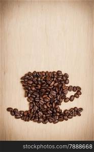 Roasted coffee beans placed in the shape of cup and saucer on wooden surface background, copy space text area