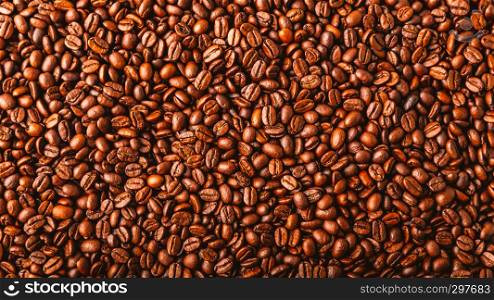 Roasted coffee beans spread over an entire surface, top view