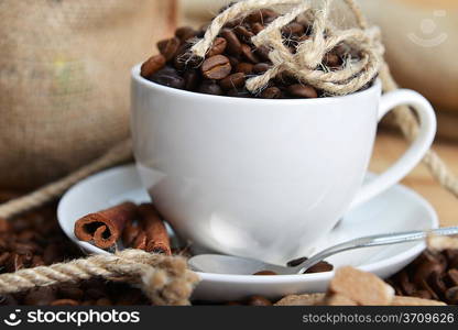 Roasted coffee beans with cup on jute hessian background