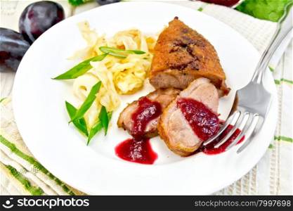 Roasted duck breast with braised cabbage, green onions and plum sauce in a white plate on a towel, plums on background light wooden boards