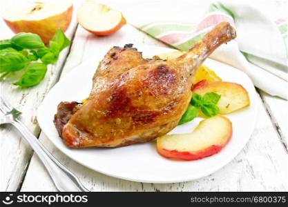 Roasted duck leg with apple, potatoes in a white plate, basil, fork and a napkin on a wooden boards background