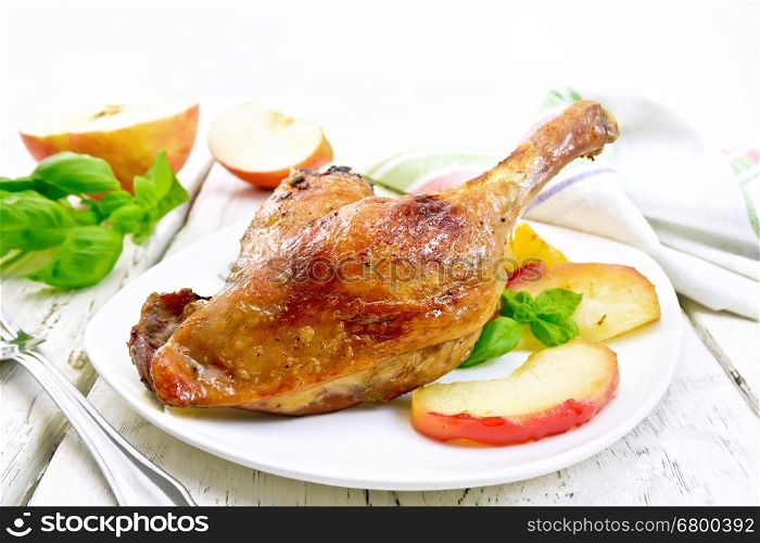 Roasted duck leg with apple, potatoes in a white plate, basil, fork and kitchen towel on a background of wooden boards