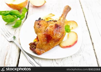 Roasted duck leg with apple, potatoes in a white plate, basil, fork and a napkin on the background light wooden boards