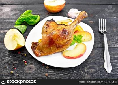 Roasted duck leg with apple, potatoes in a white plate, basil, garlic and fork on the background of wooden boards