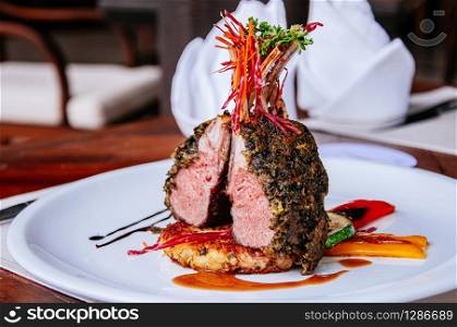 Roasted Lamb chop steak with crispy herb crust and grilled vegetables on white plate at dinner table