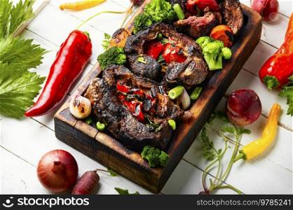 Roasted meat with vegetable garnish on cutting board. Barbecue meat with vegetables.