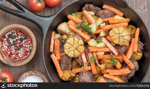 Roasted meat with vegetables in a cast iron skillet on a wooden table