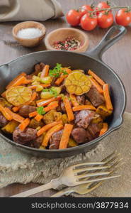 Roasted meat with vegetables in a cast iron skillet on a wooden table