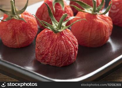 Roasted peeled red vine tomatoes with stem on a dish close up