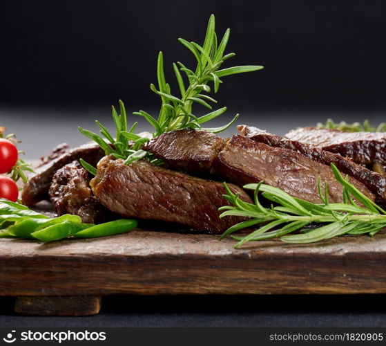 roasted piece of beef ribeye cut into pieces on a vintage brown chopping board, rare doneness. Appetizing steak