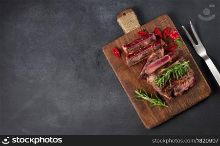 roasted piece of beef ribeye cut into pieces on a vintage brown chopping board, rare doneness. Delicious steak, copy space