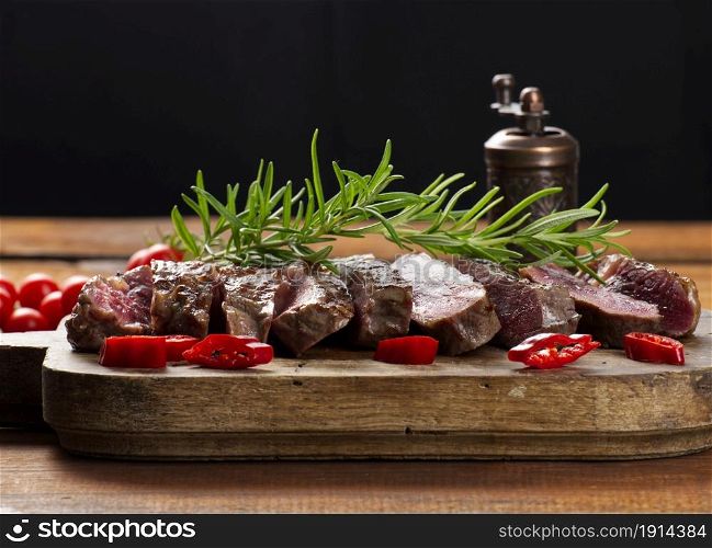 roasted piece of beef ribeye cut into pieces on a vintage brown chopping board, rare doneness. Delicious steak, close up