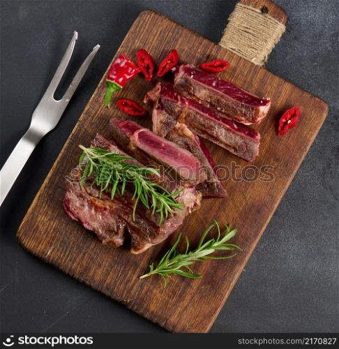 roasted piece of beef ribeye cut into pieces on a vintage brown chopping board, rare doneness. Appetizing steak on a kitchen board