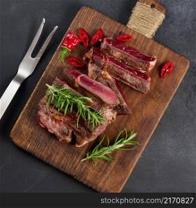 roasted piece of beef ribeye cut into pieces on a vintage brown chopping board, rare doneness. Appetizing steak on a kitchen board