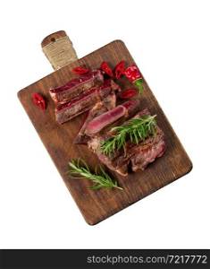 roasted piece of beef ribeye cut into pieces on a vintage brown chopping board, rare doneness. Appetizing steak on kitchen board isolated on white background