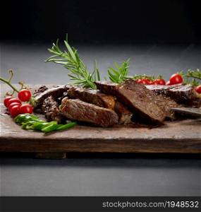 roasted piece of beef ribeye cut into pieces on a vintage brown chopping board. Delicious steak, close up