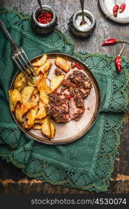 Roasted Pork fillet with a crust and baked potato in plate with fork on rustic kitchen table, top view