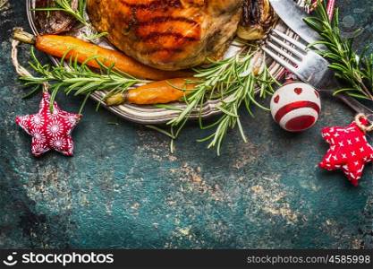 Roasted pork ham on silver plate with vegetables , cutlery and Christmas decoration, top view, border