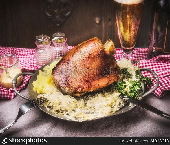 Roasted pork knuckle eisbein with mashed potatoes and braised boiled cabbage in plate with cutlery and beer on rustic table, front view. Country style