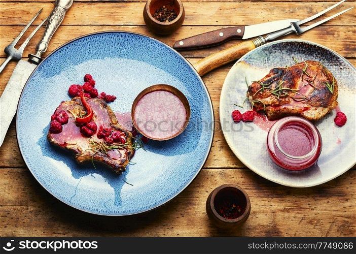 Roasted pork steak on a plate and raspberry sauce. Pork steak with berry sauce.