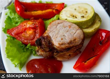 roasted pork steak with grilled vegetables on white plate