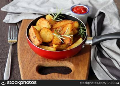 Roasted potatoes with rosemary in iron pan on rustic cutting board .. Roasted potatoes with rosemary in iron pan on rustic cutting board